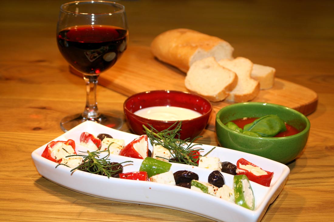 Hausgemachte Antipasti - eingelegte Oliven, Paprika mit Käsecremefüllung, eingelegter Schafskäse, Peperoni und Dips
